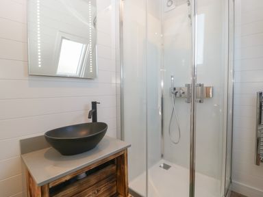 A bathroom with a black vessel sink on a wooden vanity and a glass shower enclosure at Leadon View Willow in Upleadon near Newent