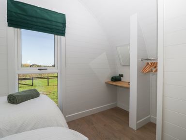 A room with two beds with green towels a window with green blind a wooden desk a mirror and a hanging rail with hangers at Leadon View Willow in Upleadon near Newent