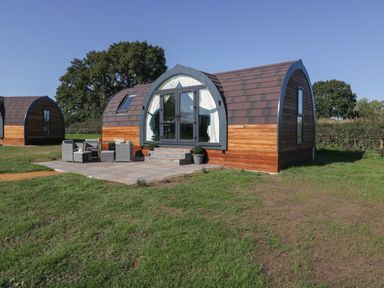 A small wooden cabin with a curved roof and patio furniture outside in a grassy area at Leadon View Willow in Upleadon near Newent