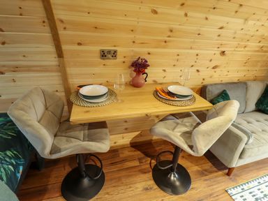 A small dining area with two chairs a wooden table set for two with plates glasses and utensils a vase with flowers and a sofa against a wooden wall at Hobhole in Keal Cotes near East Kirkby