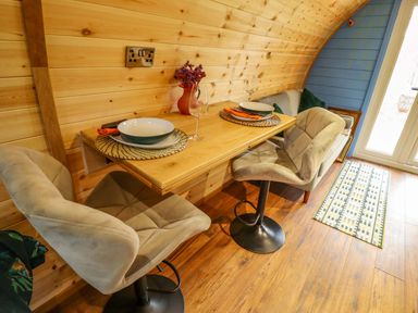 A small dining area with a wooden table set for two with chairs and a sofa in a room with wooden walls and a blue accent wall at Hobhole in Keal Cotes near East Kirkby