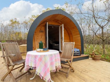 A wooden outdoor deck with a round table covered with a cloth and two wooden chairs in front of a curved wooden cabin at Hobhole in Keal Cotes near East Kirkby
