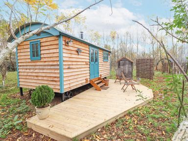 A wooden cabin with blue doors and windows on a wooden deck with chairs and a potted plant at Catchwater in Keal Cotes near East Kirkby