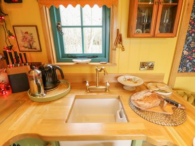 A kitchen sink with a brass faucet on a wooden countertop with a loaf of bread and a knife beside it and a kettle and coffee pot on a tray near a window at Catchwater in Keal Cotes near East Kirkby