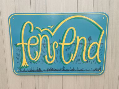 A blue sign with yellow and green decorative text reading fen end mounted on a light-colored wooden wall