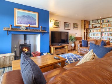 A living room with leather sofas a wooden coffee table a fireplace with a wood burning stove a television and bookshelves at Hendre in Blaenau Ffestiniog