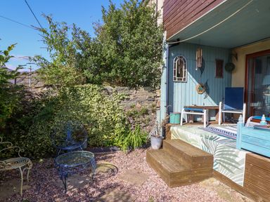 An outdoor patio area with metal chairs and a table next to wooden steps and garden plants at Hendre in Blaenau Ffestiniog