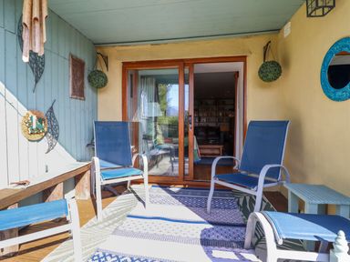 A covered outdoor seating area with blue chairs and a patterned rug by sliding glass doors at Hendre in Blaenau Ffestiniog