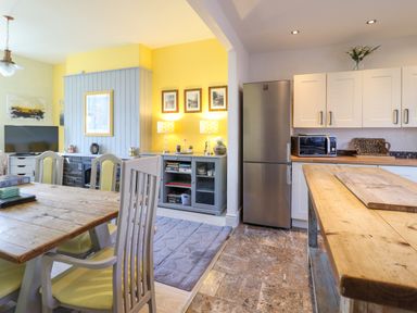 A dining area with a wooden table and chairs next to a kitchen with white cabinets and stainless steel refrigerator at Hendre in Blaenau Ffestiniog