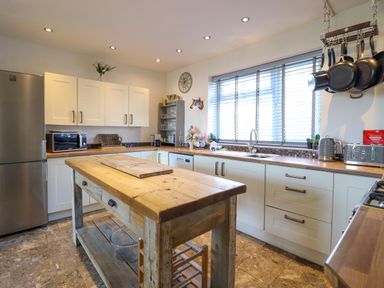 A kitchen with wooden island, white cabinets, stainless steel fridge, and hanging pots at Hendre in Blaenau Ffestiniog