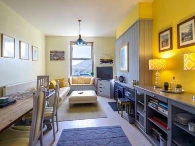 A living room and dining area with a sofa ottoman dining table chairs tv cabinet and window seat at Hendre in Blaenau Ffestiniog