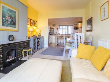 A living room with a fireplace sofa with yellow cushions dining table and chairs leading to a kitchen at Hendre in Blaenau Ffestiniog