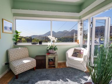 A sunroom with two chairs a small table and plants overlooking mountains at Hendre in Blaenau Ffestiniog
