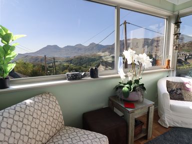 A sitting area with chairs a small table with a plant and windows showing a mountain view at Hendre in Blaenau Ffestiniog
