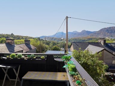 A balcony with small plants and a bench overlooking houses and mountains at Hendre in Blaenau Ffestiniog