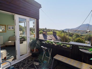 A balcony with a bench plants and a small table overlooking a rural landscape with houses and hills at Hendre in Blaenau Ffestiniog