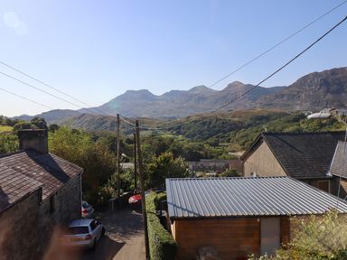 A rural street with houses trees and mountains in the background at Hendre in Blaenau Ffestiniog