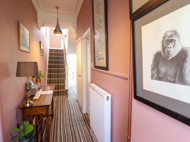 A hallway with a striped carpet leading to stairs with framed pictures on the walls and a wooden table with a lamp at Hendre in Blaenau Ffestiniog