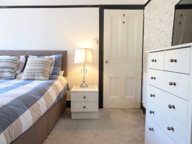 A bedroom with a bed a bedside table with a lamp a door and a white chest of drawers at Hendre in Blaenau Ffestiniog