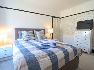 A bedroom with a double bed with striped bedding two bedside tables with lamps a chest of drawers with a television on top at Hendre Blaenau Ffestiniog