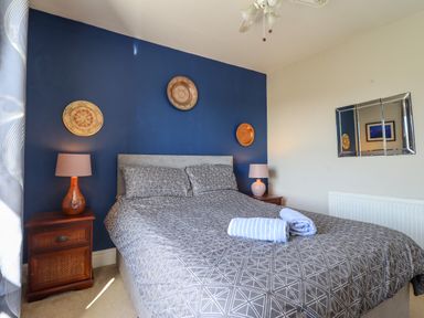 A bedroom with a bed between two wooden bedside tables with lamps and decorative plates on a blue wall at Hendre in Blaenau Ffestiniog
