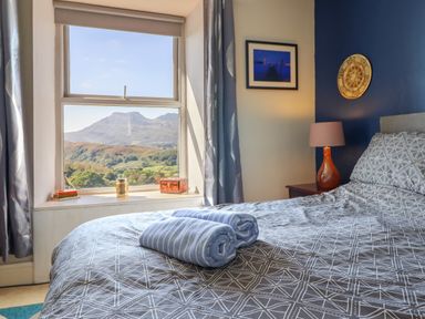 A bedroom with a bed and two rolled towels on it a window with a mountain view and a nightstand with a lamp at Hendre in Blaenau Ffestiniog