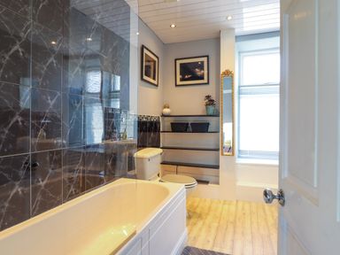 A bathroom with a bathtub toilet shelves and a window at Hendre in Blaenau Ffestiniog