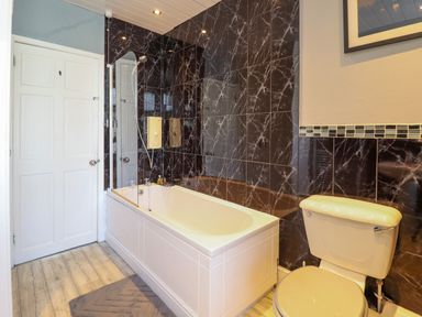 A bathroom with a white bathtub and toilet with black marble tiled walls at Hendre in Blaenau Ffestiniog
