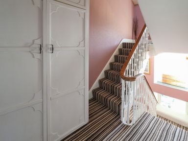 A staircase with striped carpet and a white wardrobe with handles at Hendre in Blaenau Ffestiniog