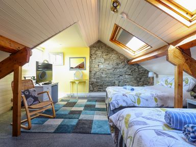 A bedroom with two beds a wooden chair a television on a cabinet and a stone wall at Hendre in Blaenau Ffestiniog