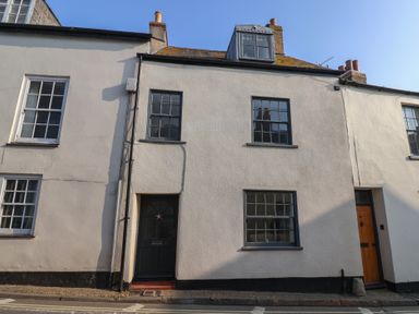 A street view of a two story white house with black framed windows and two doors at 47 Church Street in Lyme Regis