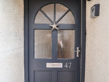 A dark blue front door with textured glass panels a silver starfish decoration house number 47 and a mail slot at 47 Church Street Lyme Regis