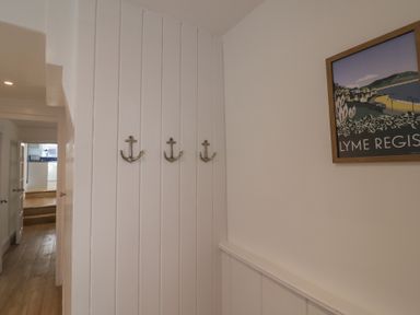 A hallway with three anchor-shaped hooks on a white panelled wall and a framed Lyme Regis poster on the adjacent wall at 47 Church Street Lyme Regis