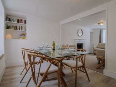 A dining area with a glass table set for six with wooden chairs next to a living room with armchairs and a fireplace at 47 Church Street in Lyme Regis
