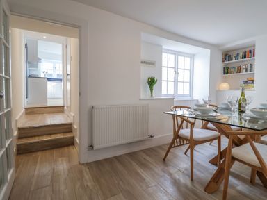 A dining room with a glass table set with dishes and glasses and wooden chairs next to a window with bookshelves in a corner at 47 Church Street Lyme Regis