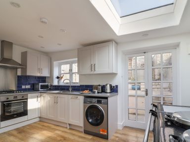 A kitchen with white cabinets blue backsplash wooden floor a washing machine and glass doors at 47 Church Street in Lyme Regis
