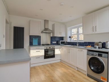 A kitchen with white cabinets, stainless steel oven, washing machine, and a window at 47 Church Street in Lyme Regis