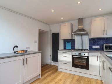 A kitchen with white cabinets a built-in oven stovetop and range hood and a countertop with a coffee press and croissants at 47 Church Street in Lyme Regis