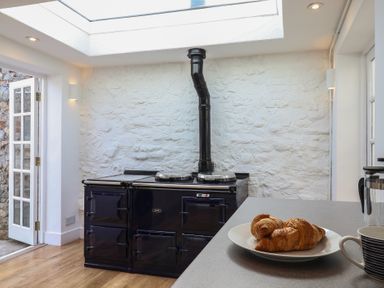 A kitchen with a black Aga stove next to a stone wall and a countertop with croissants and a cup at 47 Church Street Lyme Regis