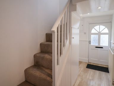 A hallway with carpeted stairs and a white front door with frosted glass at 47 Church Street in Lyme Regis