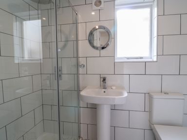 A bathroom with a glass shower enclosure a pedestal sink with a bar of soap a round mirror a window and a toilet at 47 Church Street in Lyme Regis