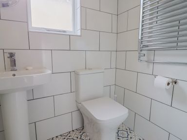 A bathroom with a toilet, a pedestal sink, tiled walls, a window, a towel radiator, and a toilet paper holder at 47 Church Street in Lyme Regis