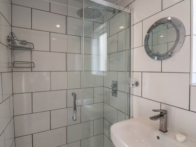 A bathroom with a glass shower enclosure a round mirror and a sink with a faucet at 47 Church Street in Lyme Regis