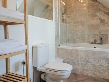 A bathroom with a toilet wooden shelf with towels and a bathtub with tiled walls at 47 Church Street in Lyme Regis