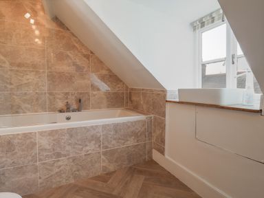 A bathroom with a bathtub, tiled walls, a window, and a sink with a countertop at 47 Church Street Lyme Regis