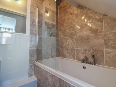 A bathroom with a bathtub and glass shower screen with tiled walls at 47 Church Street Lyme Regis