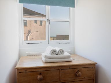 A wooden dresser with folded white towels on top in front of a window at 47 Church Street in Lyme Regis