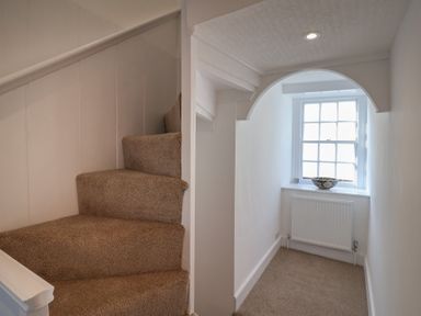 A carpeted staircase next to a small hallway with a window and a decorative bowl on the windowsill at 47 Church Street in Lyme Regis