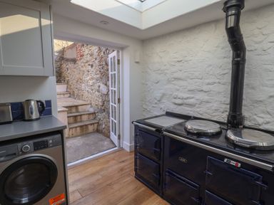 A kitchen with a washing machine counter appliances and a black stove near an open door with stone stairs at 47 Church Street in Lyme Regis