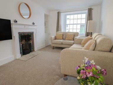 A living room with two beige sofas cushions fireplace TV and flowers on a table at 47 Church Street in Lyme Regis